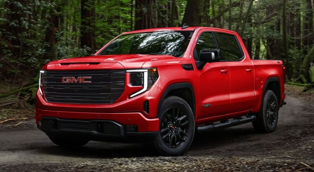 A red 2024 GMC Sierra 1500 Elevation is driving on a dirt road after leaving a GMC dealer.