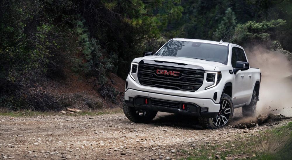 A white 2024 GMC Sierra 1500 AT4 is off-roading on a rocky trail after leaving a GMC dealer.