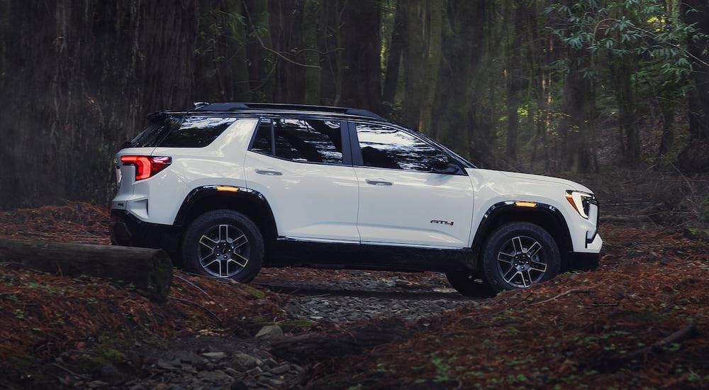 Side of a white 2026 GMC Terrain driving through a forest.