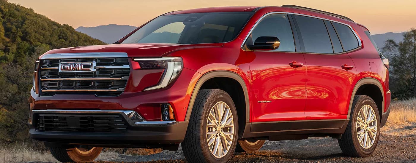 Red 2026 GMC Acadia parked off-road on gravel.