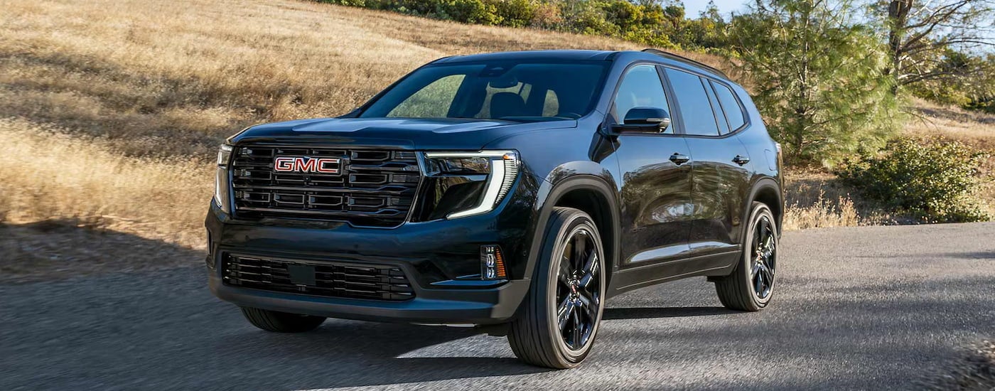Black 2026 GMC Acadia driving on a trail.