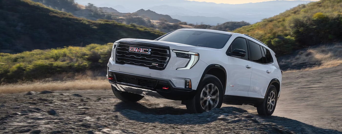 White 2026 GMC Acadia driving off-road up a hill.
