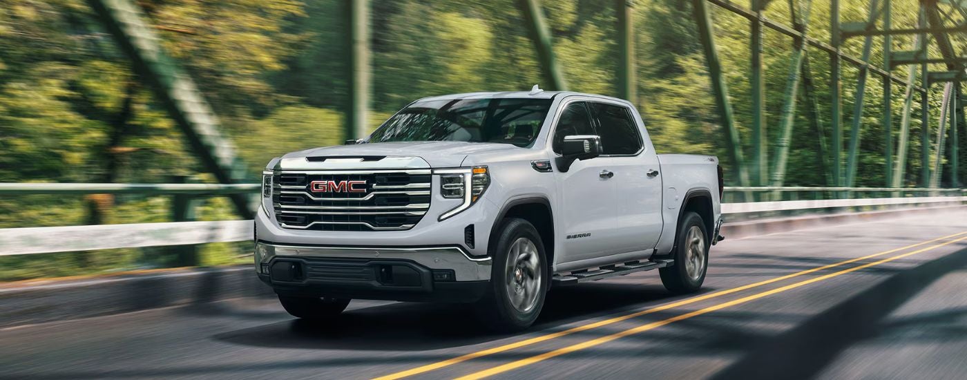 White 2026 GMC Sierra 1500 driving over a bridge in the sunlight.