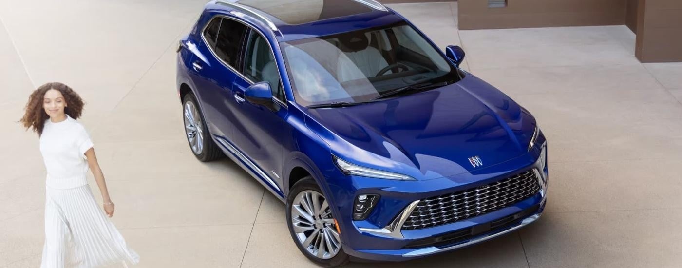 A blue 2025 Buick Envision for sale is parked on concrete as a woman walks by.