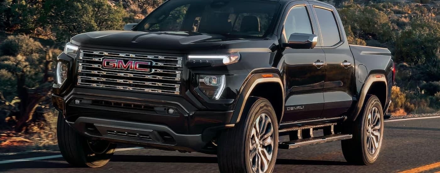 A black 2024 GMC Canyon Denali is driving on an open road after leaving a GMC dealer.