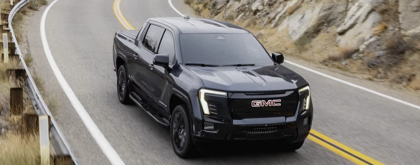 A black 2025 GMC Sierra EV Elevation driving on a highway after visiting a GMC dealer near Sterling